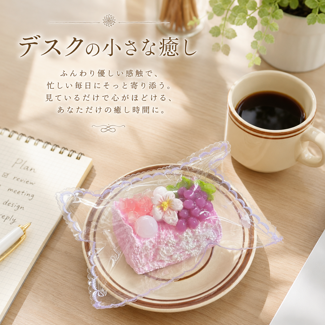 Cake squishy toy on a plate on a wooden desk beside a coffee cup, open notebook, and potted plant