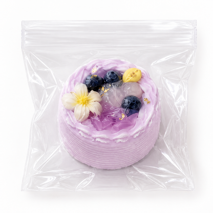 Purple blueberry and floral decorated mini cake squishy stress relief toy wrapped in clear plastic on a white surface.