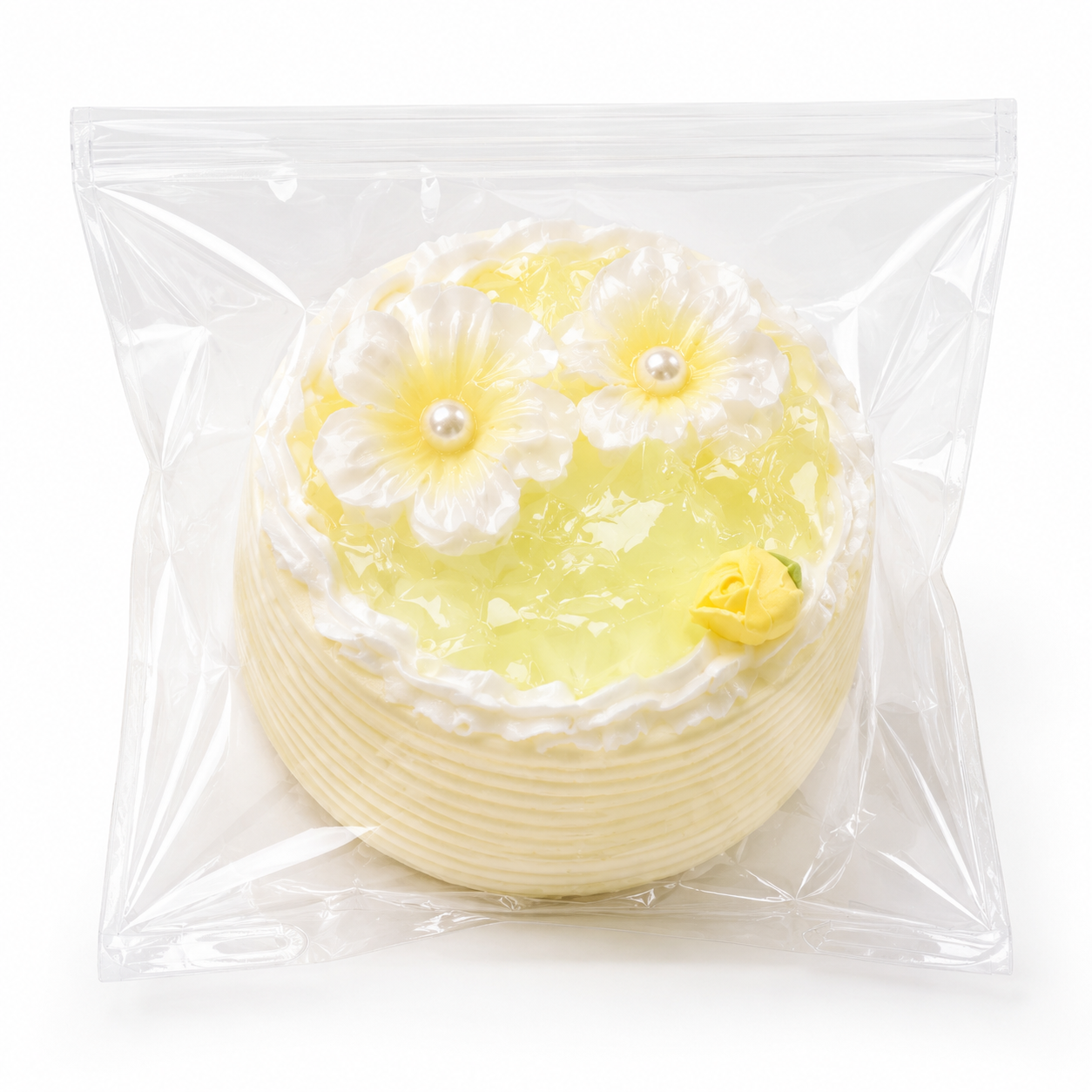 Light yellow lemon style mini cake squishy toy adorned with white flowers and pearls inside a clear ziplock bag.