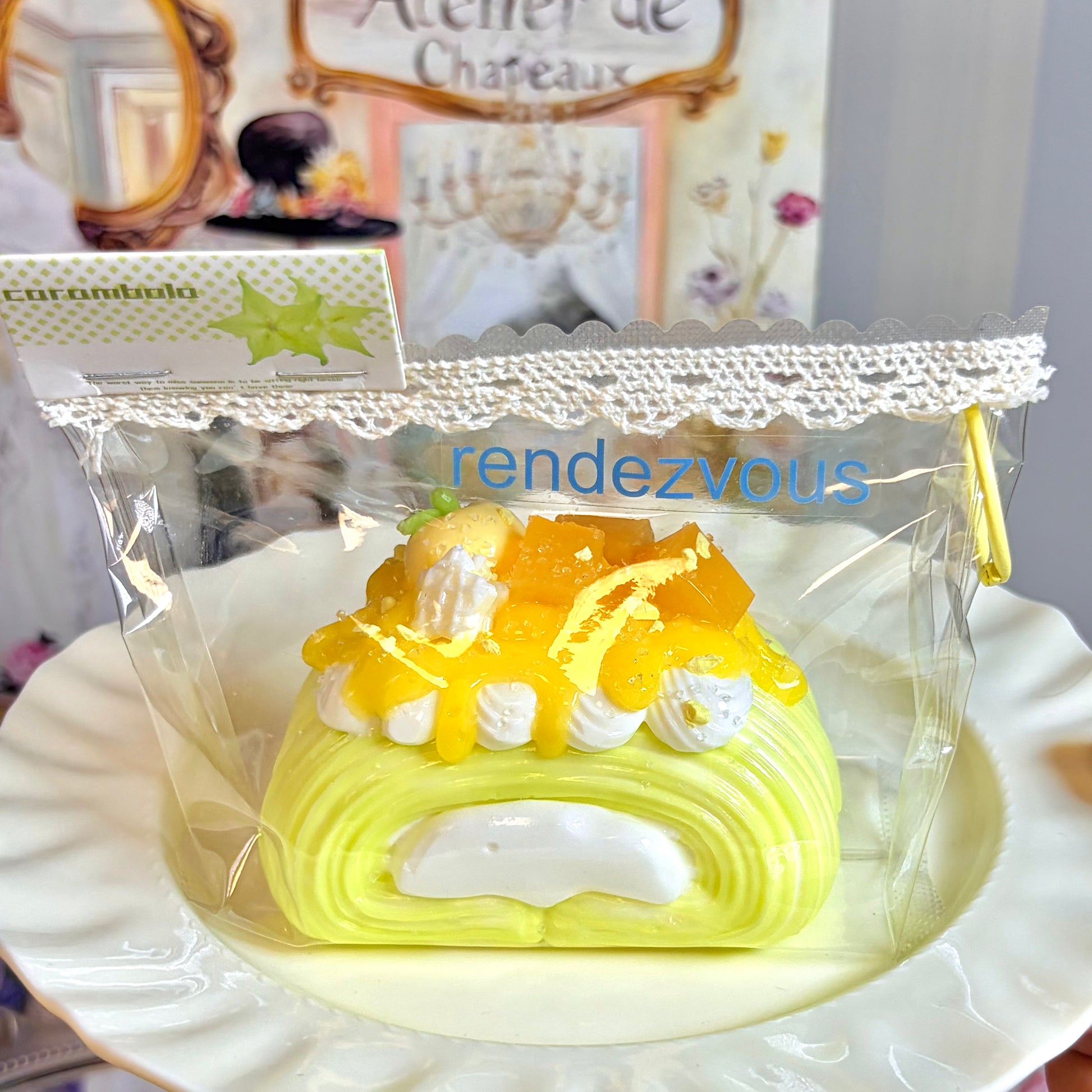 Yellow mango Swiss roll squishy with white faux cream and glossy syrup, in a clear pouch with lace trim and a star-shaped paper tag on a wavy white plate