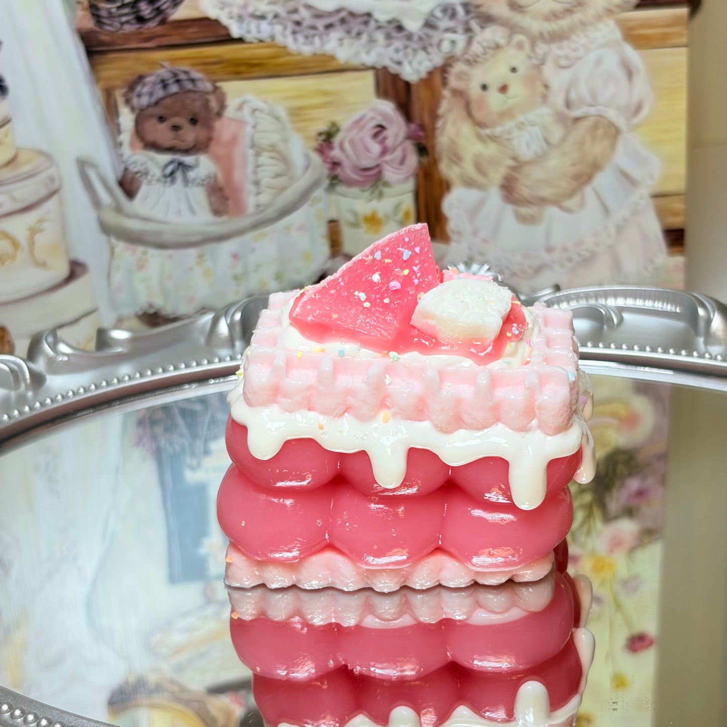 Square pink layer cake squishy with watermelon topping and white icing drips on a reflective surface.