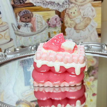 Square pink layer cake squishy with watermelon topping and white icing drips on a reflective surface.