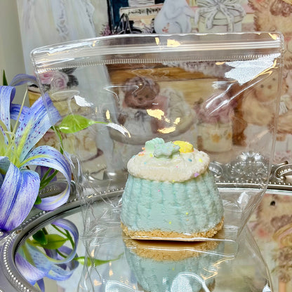 Blue pastel squishy dessert toy with star decorations packaged in a clear bag next to a blue lily.