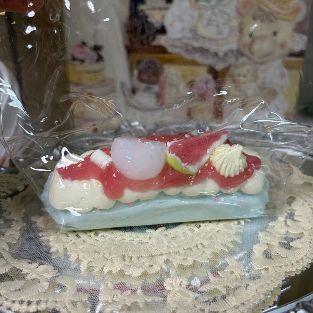 Blue pastry-shaped squishy toy with cream and fruit toppings resting on a white lace doily in clear packaging.