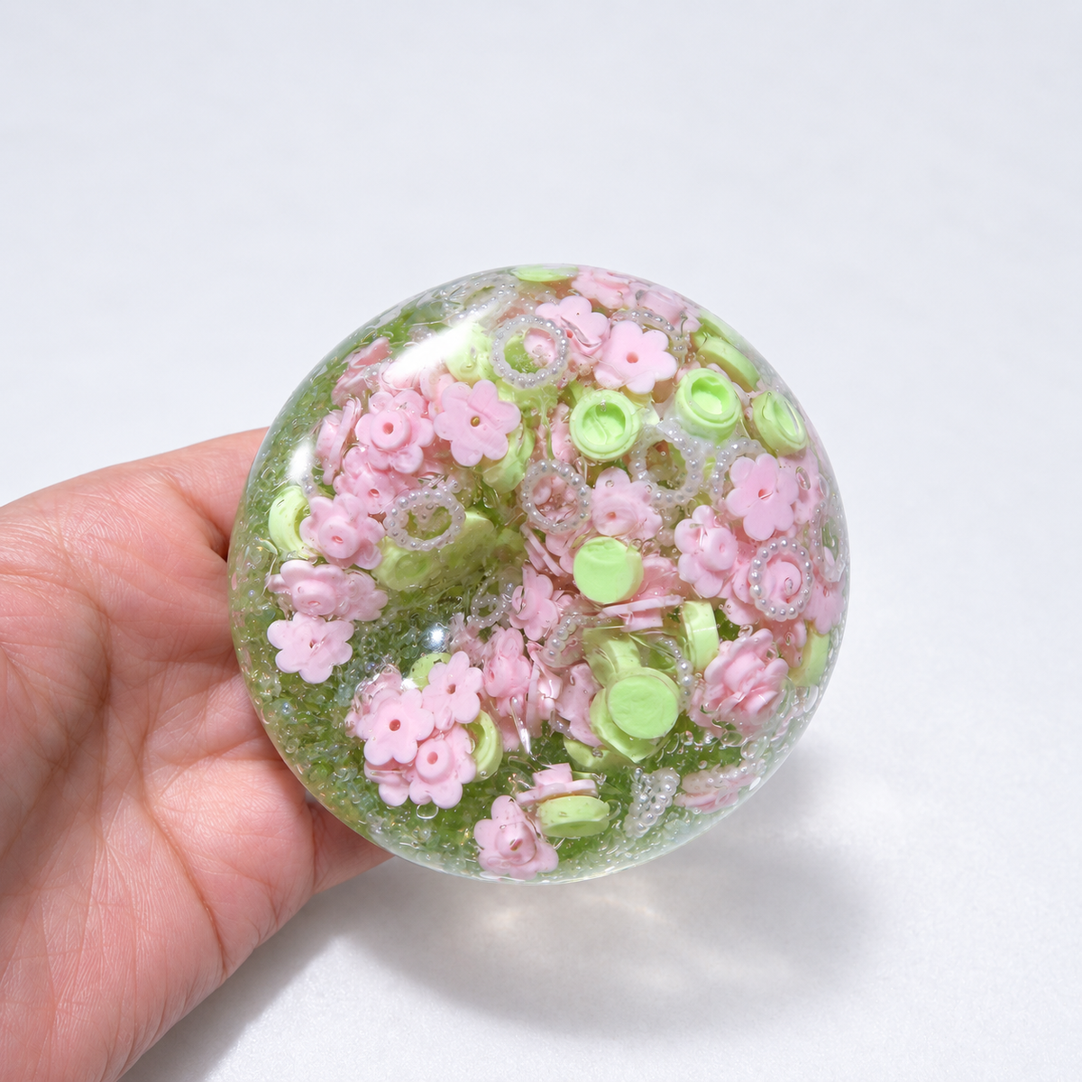 Green-tinted sensory squishy ball with resin pink flower-shaped pieces and small decorative beads; Spring Blossom handmade sensory squishy ball, product photo 1