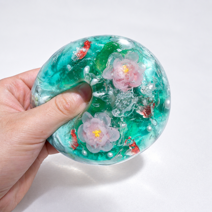 Teal sensory squishy ball with resin lotus-inspired flowers and small koi-shaped details; Koi Plays Among Lotus handmade sensory squishy ball, product photo 2