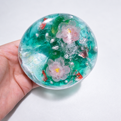 Teal sensory squishy ball with resin lotus-inspired flowers and small koi-shaped details; Koi Plays Among Lotus handmade sensory squishy ball, product photo 3