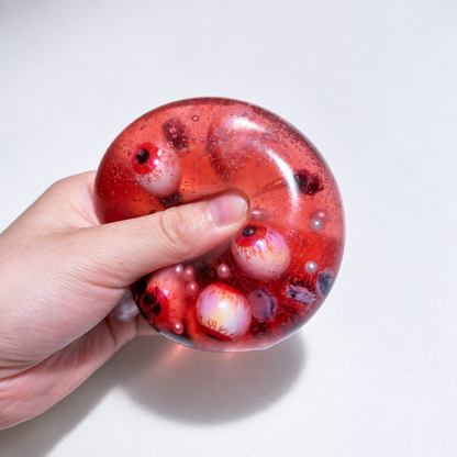 A hand squeezing the red eyeball sensory ball