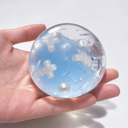 Translucent blue sensory ball with resin cross and pearl details held in a hand