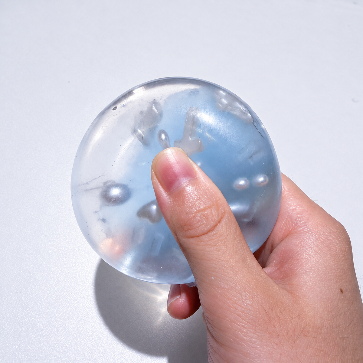 A hand pressing the translucent blue ball with cross and pearl details