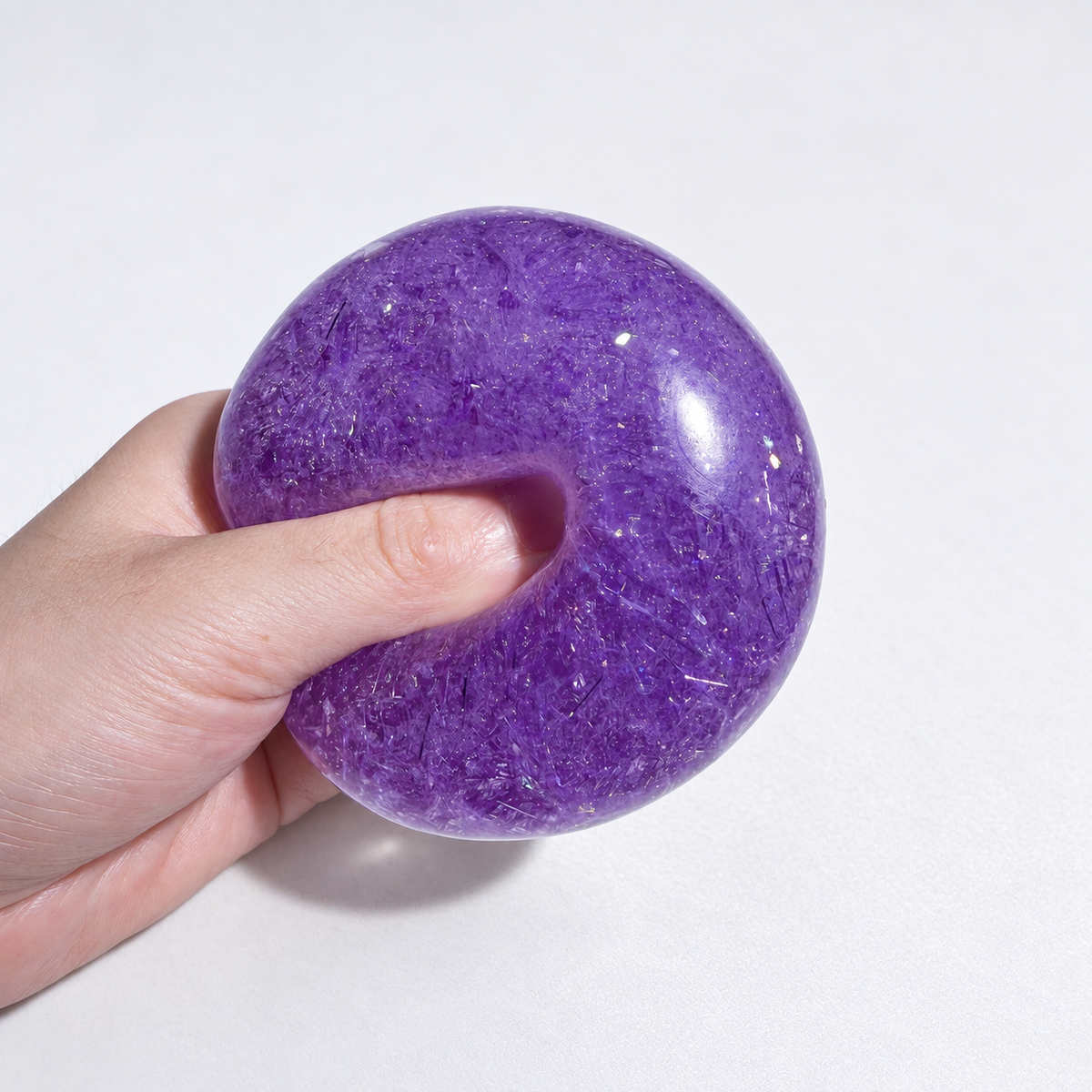 A hand squeezing the purple ball with transparent inclusions