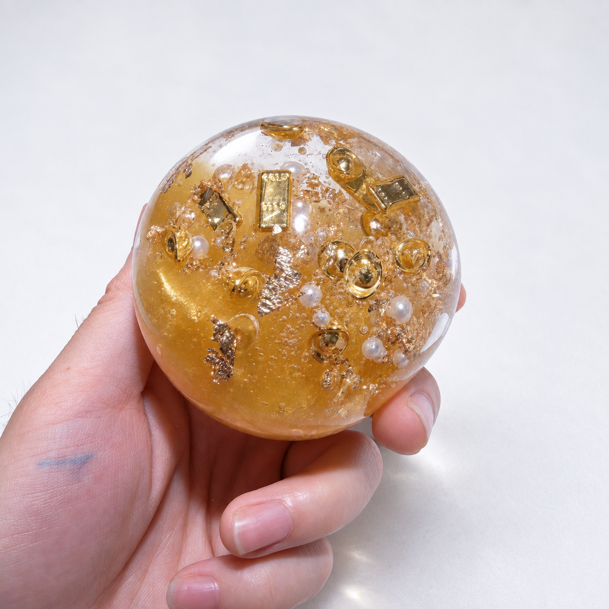 Amber-gold sensory ball with resin gold-bar and pearl details held in a hand