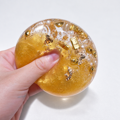 A hand pressing the amber ball with resin gold-bar and pearl inclusions