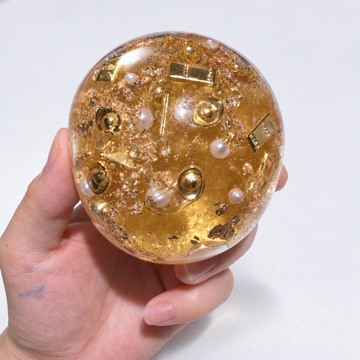 Amber-gold ball held in a hand, showing its gold-themed inclusions